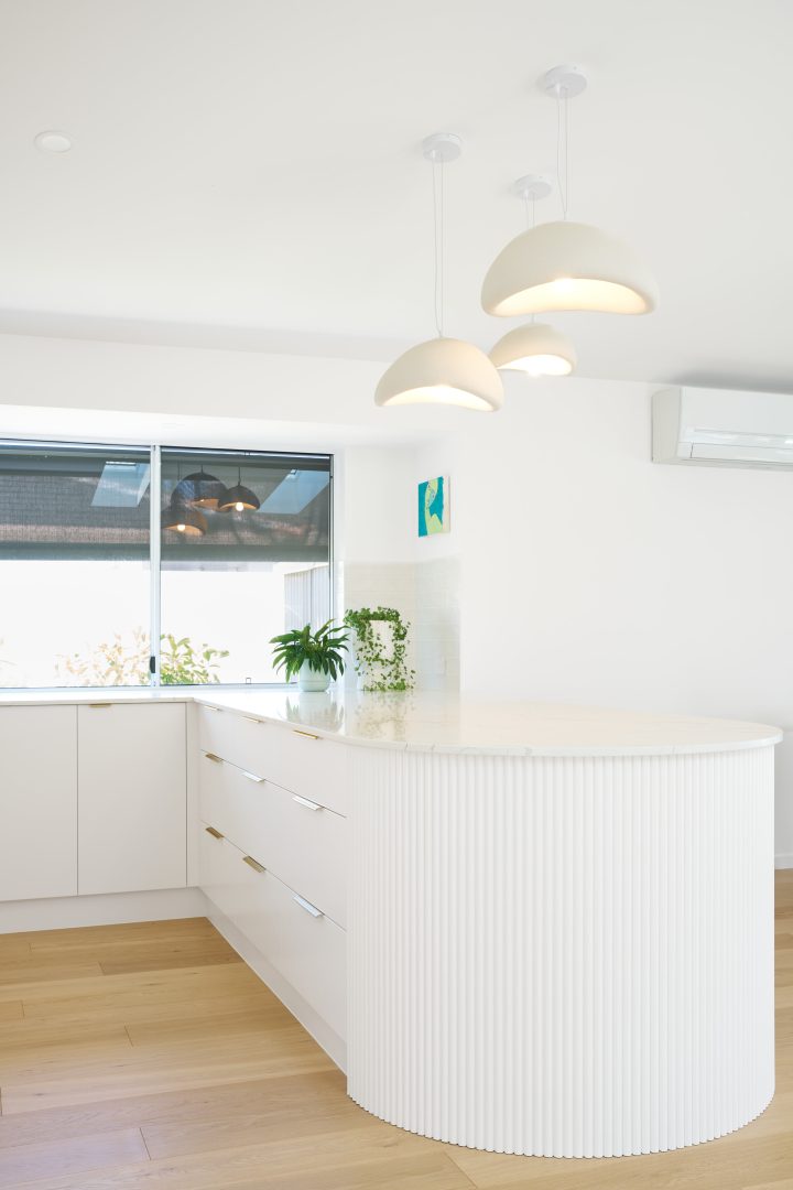 Modern white kitchen with curved island and pendant lights.